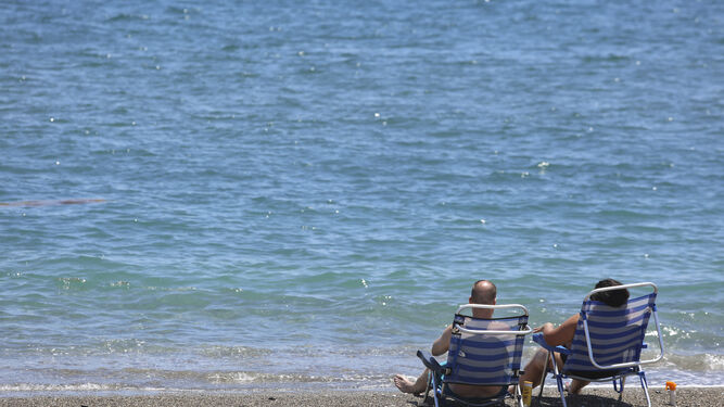 Dos personas, sentadas frente a la orilla del mar en Málaga.