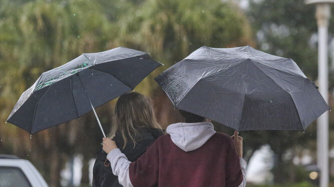 Dos jóvenes se protegen de la lluvia este viernes en Málaga.