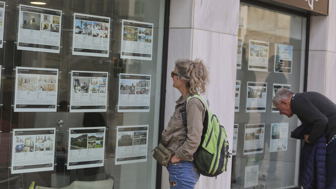 Dos personas miran los carteles del escaparate de una inmobiliaria.