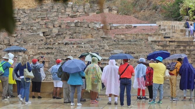 Un grupo de turistas se protege de la lluvia frente al Teatro Romano de Málaga.