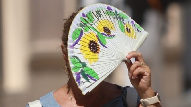 Una mujer se resguarda del sol tras su abanico.