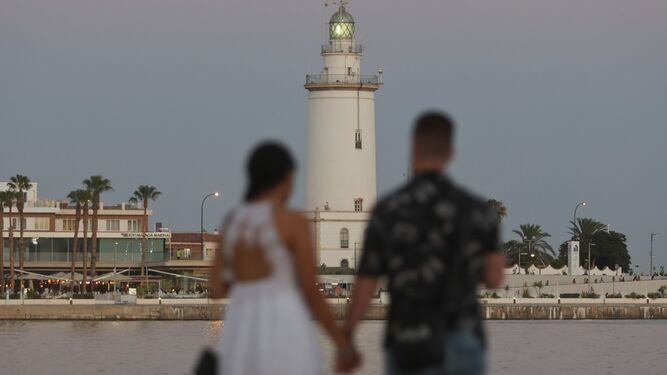 Una pareja pasea por el Puerto de Málaga, con la Farola de fondo.