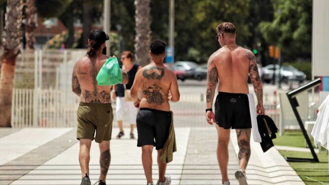 Tres jóvenes sin camiseta pasean por Málaga.