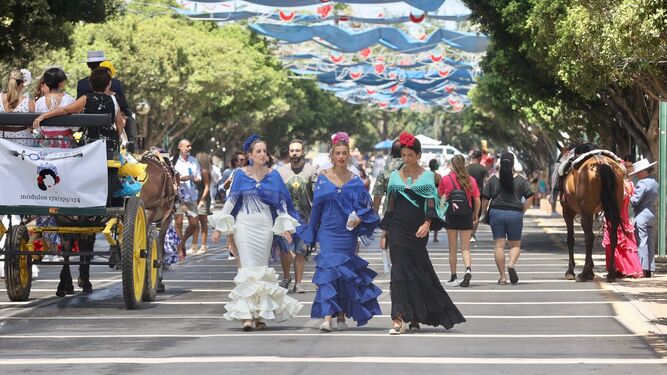 Tres chicas vestidas de flamenca pasean por el Real.