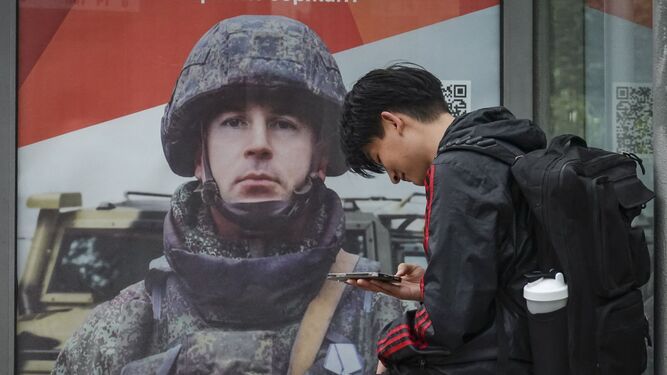 Un ruso espera en una parada de bus en Moscú con anuncios de reclutamiento al fondo