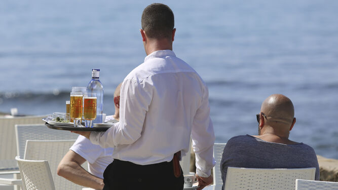 Un camarero atiende a unos clientes en un local de restauración cercano a la playa.