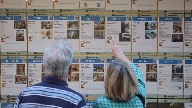 Dos personas revisan el escaparate de una agencia inmobiliaria en Málaga.