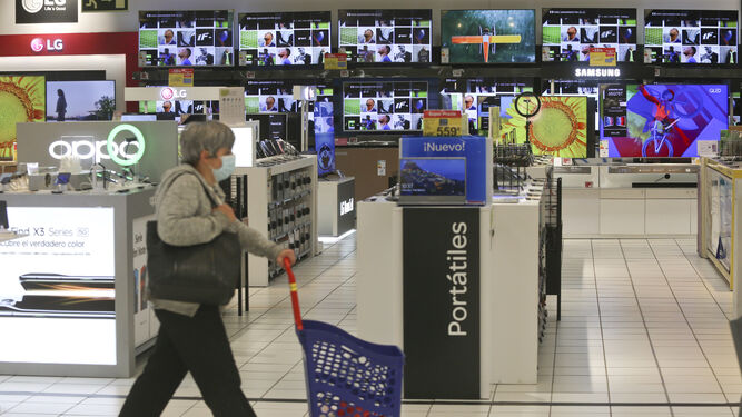 Mujer pasando por el pasillo de las televisiones en un supermercado.