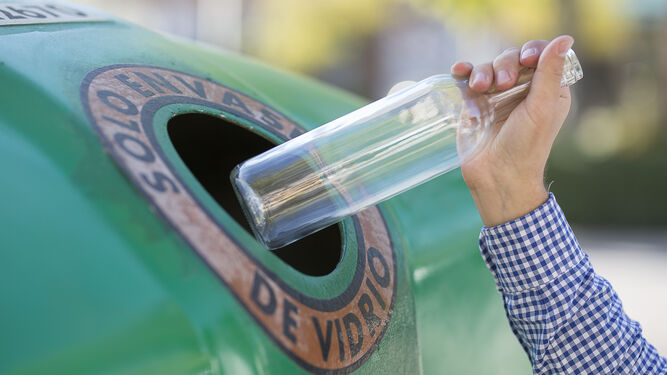 Una persona deposita un envase de vidrio en el contenedor verde