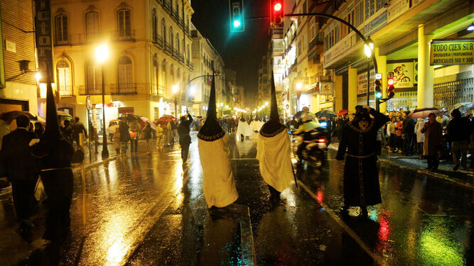 Nazarenos bajo la lluvia durante la Semana Santa en calle Victoria