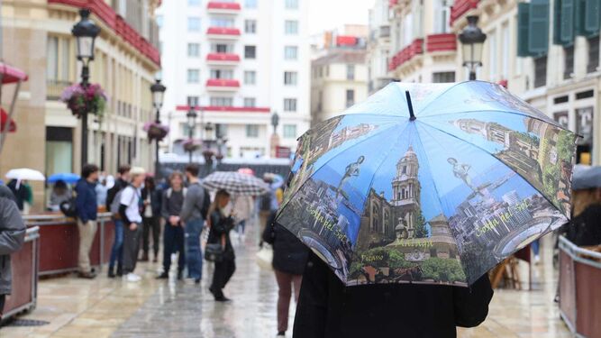 Una persona camina por la calle Larios con un paraguas con motivos malagueños.