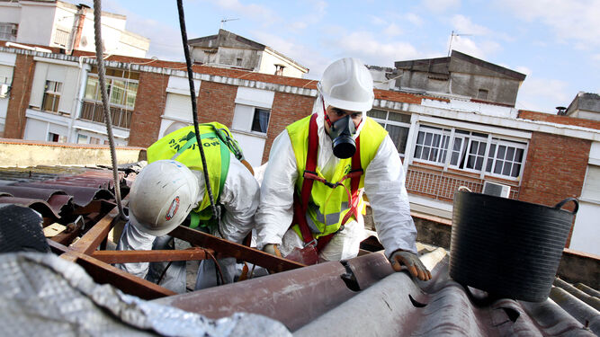 Dos operarios realizan labores de recogida de placas con amianto en un tejado.