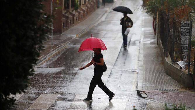 Dos personas caminan con sus paraguas en Huelva.